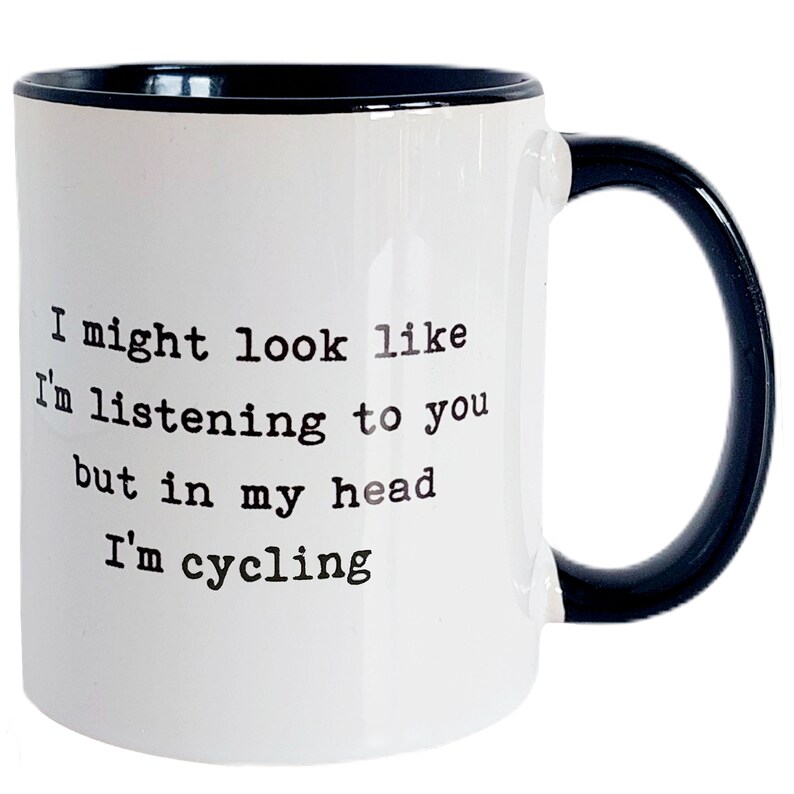 May include: White ceramic mug with a black interior and handle. The mug features the text "I might look like I'm listening to you but in my head I'm cycling" in black, sans-serif font.