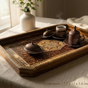 Puede incluir: Una bandeja de servicio rectangular de madera con intrincados patrones de marquetería geométrica y floral. La bandeja mide 45 x 30,5 x 4 cm y contiene dos recipientes metálicos con tapa y una taza pequeña con plato, todos con grabados.