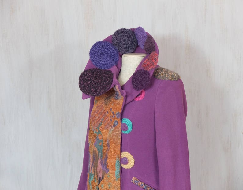 May include: A purple jacket with a colorful crocheted collar and a patterned fabric scarf. The jacket has a variety of colorful crocheted circles sewn on the front.