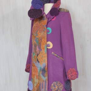 May include: A long purple coat with a colorful crocheted collar and trim. The coat has a unique design with a patterned fabric panel on one side.