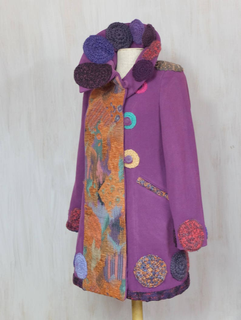 May include: A long purple coat with a colorful crocheted collar and trim. The coat has a unique design with a patterned fabric panel on one side.
