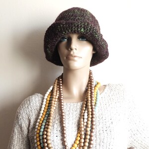 May include: A mannequin wearing a brown and green crocheted hat and a multi-strand necklace of wooden beads in shades of brown, white, and yellow.