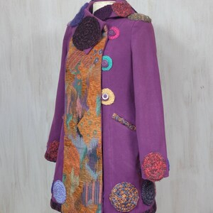 May include: A purple coat with a colorful crocheted trim and buttons. The coat has a patchwork design on one side and a solid color on the other.