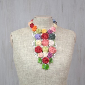 Pu&ograve; includere: Una collana di fiori di stoffa colorati con perline verdi. La collana &egrave; esposta su un manichino di stoffa bianca.