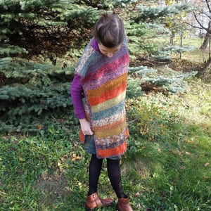 May include: A colorful striped crochet poncho with a long, flowing design. The poncho is made with a variety of different colored yarns, including orange, red, green, blue, and brown.