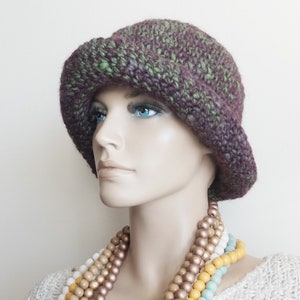 May include: A purple and green crocheted hat with a wide brim. The hat is worn by a mannequin with a multi-colored beaded necklace.