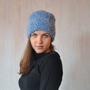 May include: A woman wearing a blue fuzzy knit beanie hat and a black sweater.
