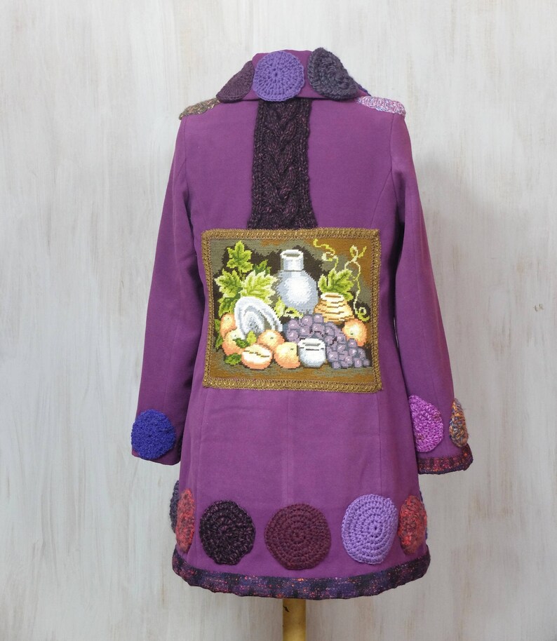 May include: Purple jacket with a crocheted collar and trim. The back of the jacket features a framed embroidered image of a still life with fruit and a vase.