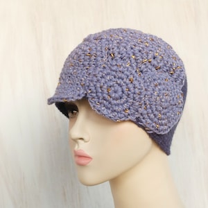 May include: A purple crocheted hat with gold accents. The hat has a wide brim and a unique design.