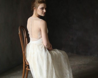 May include: A woman wearing a white wedding dress with a lace bodice and a sheer back. She is sitting on a wooden chair against a dark background. The text "designer: Anna Skoblikova" and "http://annaskoblikova.com" is visible at the bottom of the image.