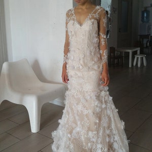 May include: A white lace wedding dress with long sleeves and a fitted bodice. The dress features delicate floral appliques and a flowing skirt.