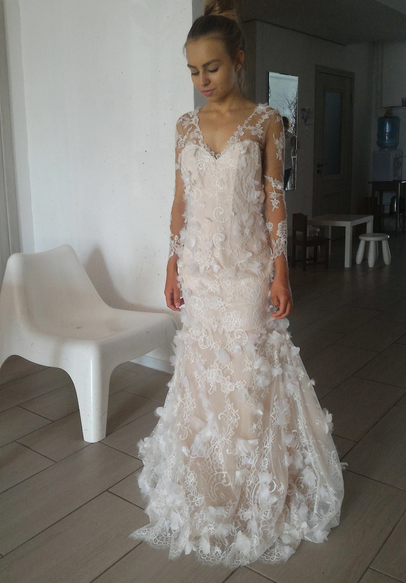 May include: A white lace wedding dress with long sleeves and a fitted bodice. The dress features delicate floral appliques and a flowing skirt.
