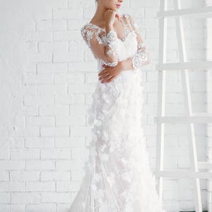 May include: A white wedding dress with a lace bodice and a flowing skirt. The dress is adorned with delicate floral appliques.
