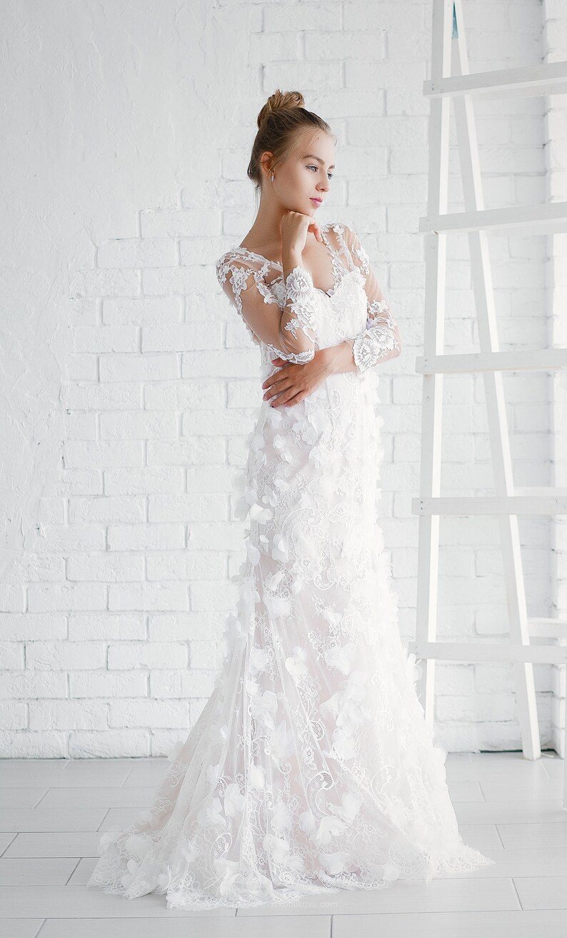 May include: A white wedding dress with a lace bodice and a flowing skirt. The dress is adorned with delicate floral appliques.