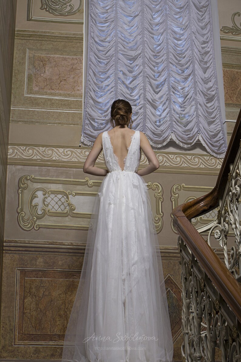 May include: A woman in a white lace wedding dress with a low back stands on a staircase in a room with ornate walls and a window with white curtains. The text "Anna Skoblikova" and "http://annaskoblikova.com" is visible at the bottom of the image.