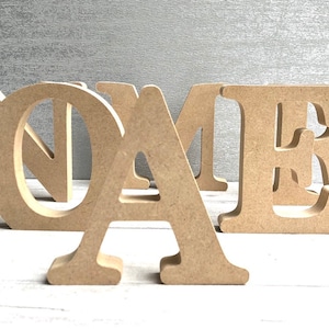 May include: Wooden letters spelling out the word "NAME" in a light brown colour. The letters are freestanding and have a slightly distressed finish.