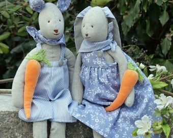 Könnte beinhalten: Zwei Plüschhasen, die blaue und weiße gemusterte Kleidung tragen. Ein Hase hält eine Karotte in seiner rechten Pfote. Die Hasen sitzen auf einer Steinoberfläche.