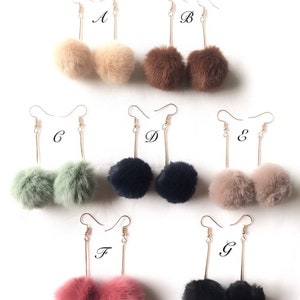 May include: Seven pairs of dangle earrings with faux fur pom poms. The pom poms are in various colors, including beige, brown, green, black, and pink. The earrings are labeled A through G.