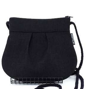 Pu&ograve; includere: Una borsa a tracolla in tessuto nero plissettato con chiusura a zip e un lungo cinturino in corda nera. La borsa ha una piccola etichetta bianca che dice "WONDERFUL IDEA".