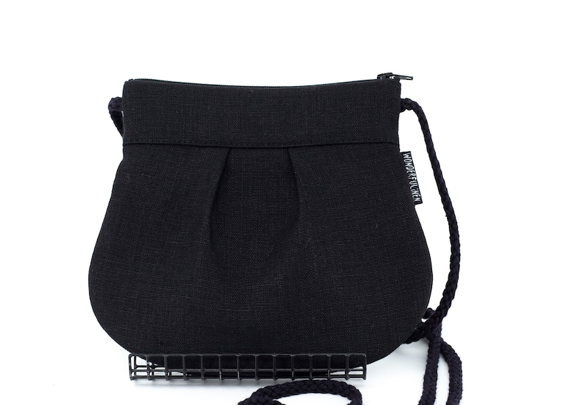 Pu&ograve; includere: Una borsa a tracolla in tessuto nero plissettato con chiusura a zip e un lungo cinturino in corda nera. La borsa ha una piccola etichetta bianca che dice "WONDERFUL IDEA".