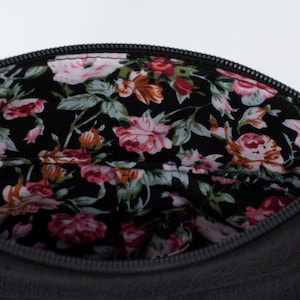 Pu&ograve; includere: Una pochette nera con cerniera e fodera floreale. La fodera presenta un motivo floreale rosa, rosso e bianco su sfondo nero.