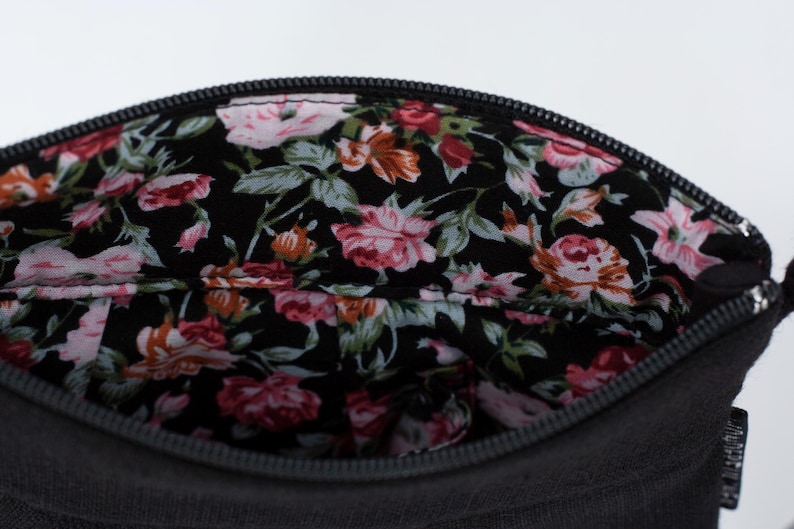 Pu&ograve; includere: Una pochette nera con cerniera e fodera floreale. La fodera presenta un motivo floreale rosa, rosso e bianco su sfondo nero.