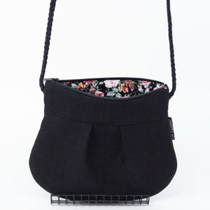 Pu&ograve; includere: Una borsa a tracolla in tessuto nero con fodera a stampa floreale. La borsa ha una chiusura a zip e un design plissettato.