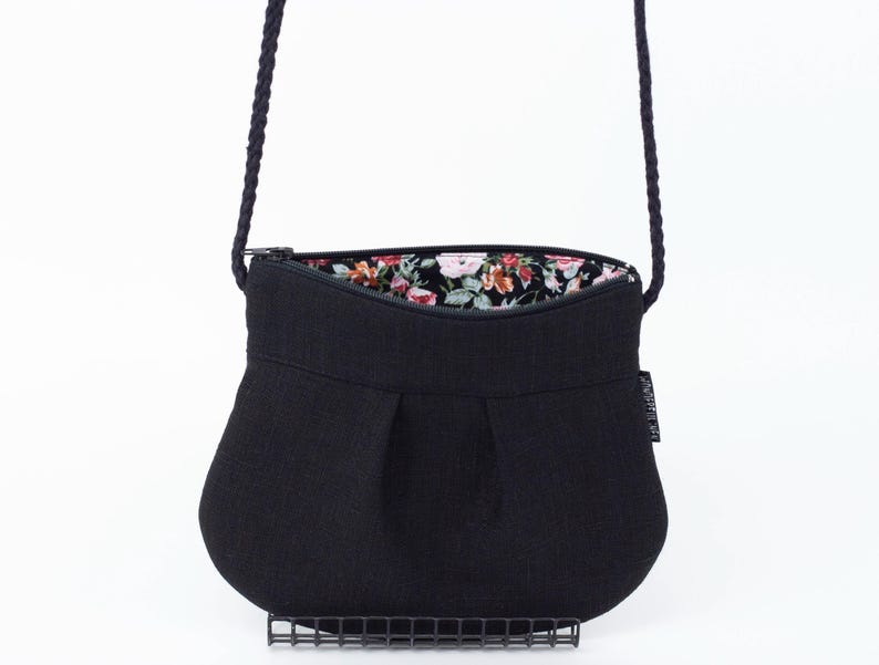 Pu&ograve; includere: Una borsa a tracolla in tessuto nero con fodera a stampa floreale. La borsa ha una chiusura a zip e un design plissettato.