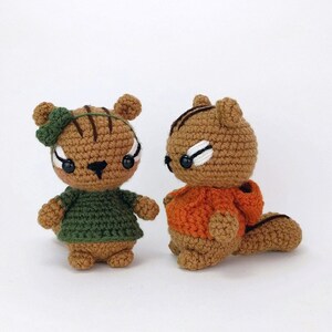 May include: Two crocheted squirrel plushies, one wearing a green shirt and the other wearing an orange shirt.
