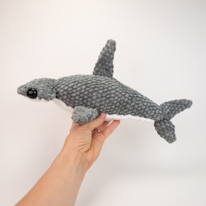 May include: Gray crocheted hammerhead shark plush toy with white belly and black eyes.