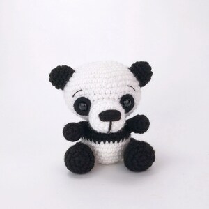 May include: A small crocheted panda bear toy with black and white fur. The panda has black eyes, a black nose, and a black stripe around its middle.