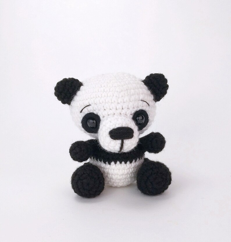 May include: A small crocheted panda bear toy with black and white fur. The panda has black eyes, a black nose, and a black stripe around its middle.