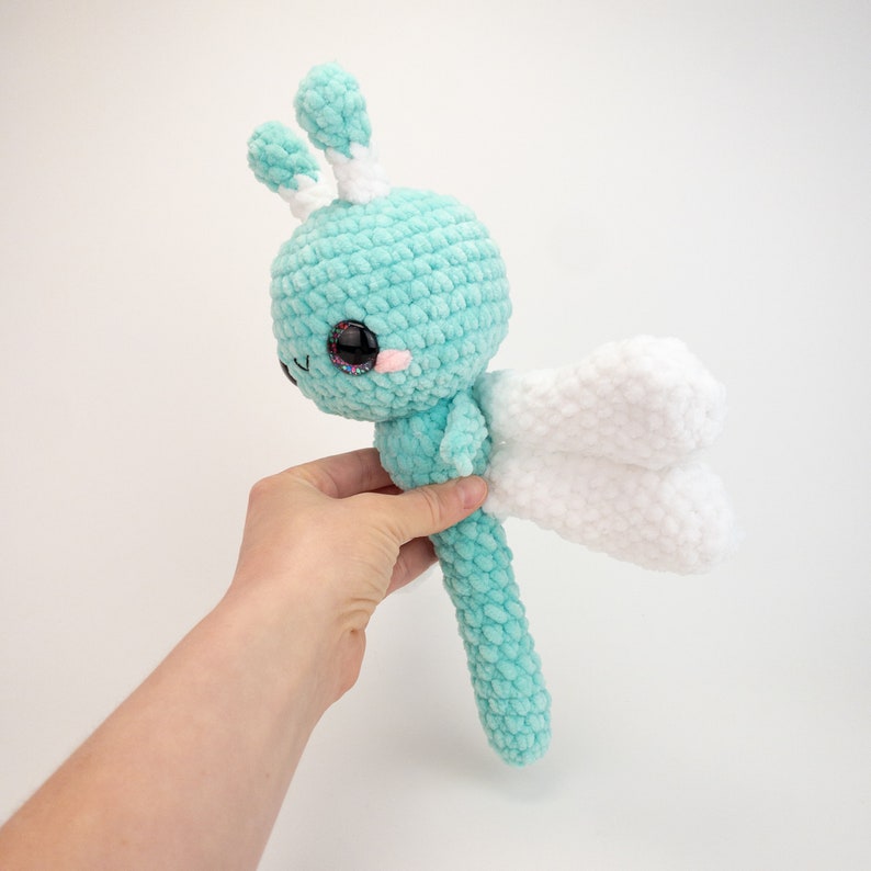 May include: A crocheted turquoise and white butterfly plush toy with large black eyes. The toy has a long body and white wings.