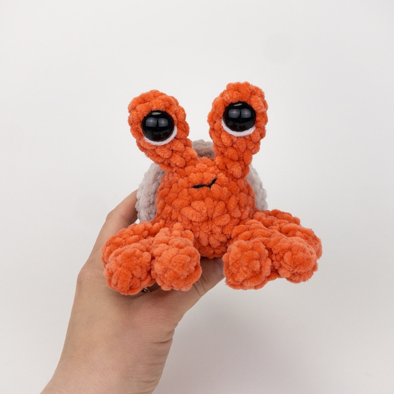 Może przedstawiać: Pluszowa zabawka w kształcie raka pustelnika, wykonana na szydełku w kolorze pomarańczowym i białym, z dużymi czarnymi oczami.