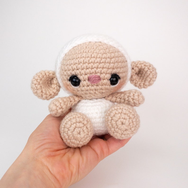 May include: A crocheted lamb toy with a white body and brown legs and ears. The lamb has black eyes and a pink nose.