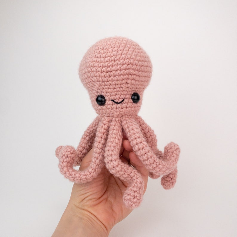May include: A pink crocheted octopus with black eyes and a smiling mouth. The octopus has eight tentacles.