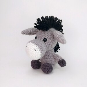 May include: A gray crocheted donkey toy with black yarn for the mane and tail. The donkey has white yarn for the muzzle and black button eyes.