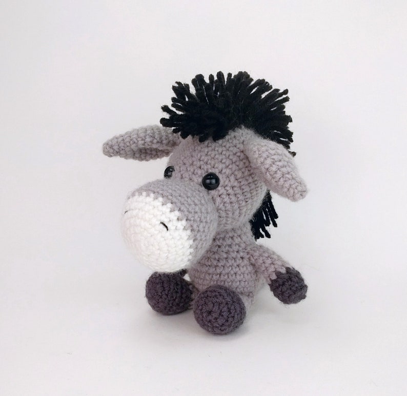May include: A gray crocheted donkey toy with black yarn for the mane and tail. The donkey has white yarn for the muzzle and black button eyes.