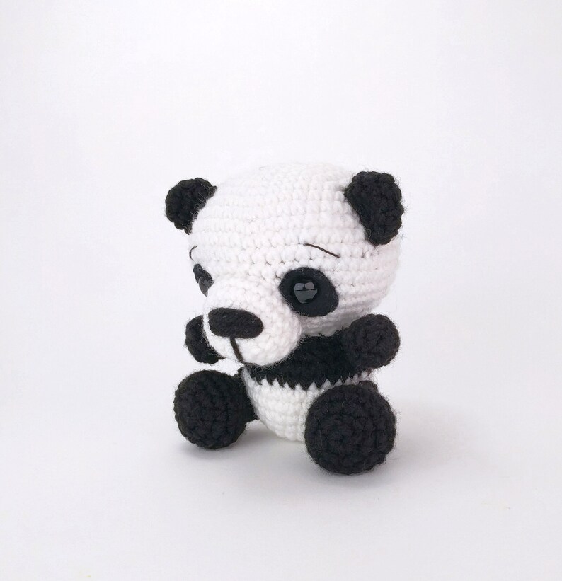 May include: A small crocheted panda bear toy with black ears, eyes, and paws. The panda is sitting with its legs crossed and has a black and white striped body.