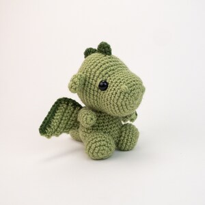 May include: A green crocheted dragon with black eyes and a small wing on one side.