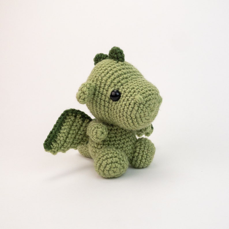 May include: A green crocheted dragon with black eyes and a small wing on one side.