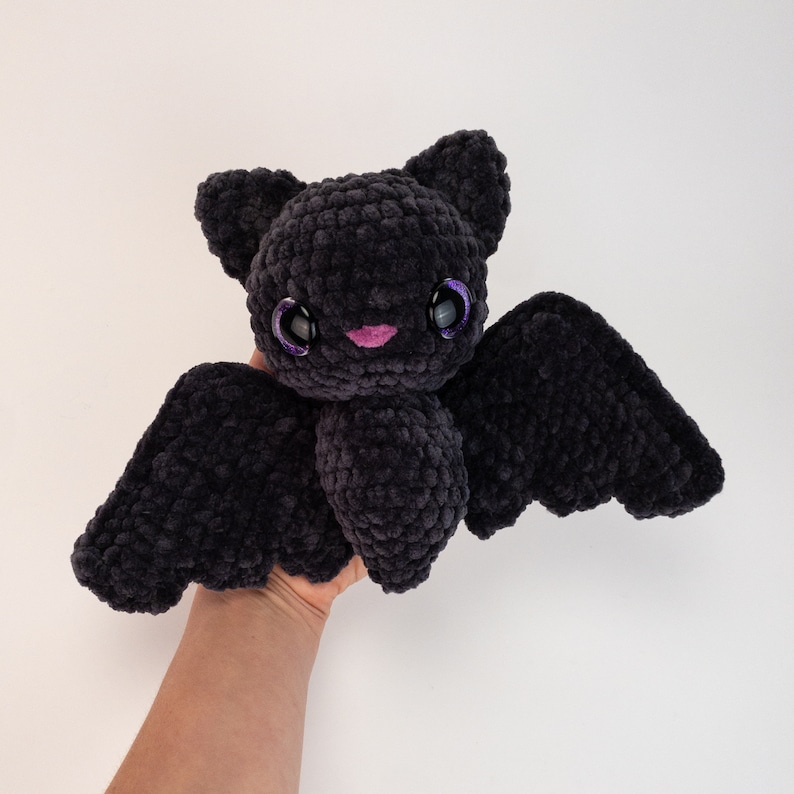 K&ouml;nnte beinhalten: Ein schwarzes, geh&auml;keltes Fledermaus-Pl&uuml;schtier mit glitzernden lila Augen und einem rosa Mund.