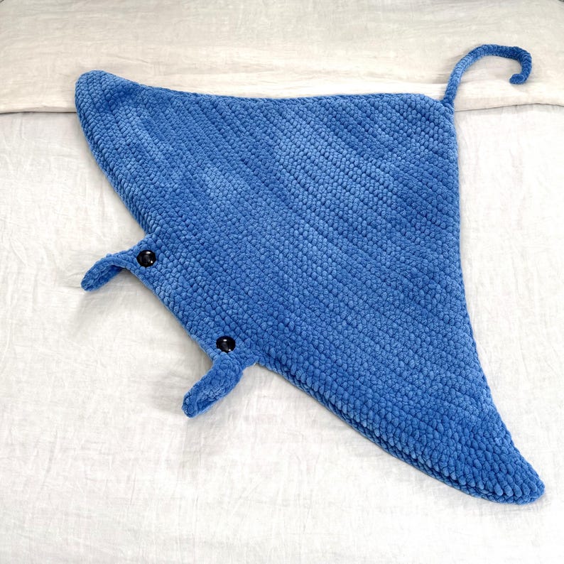 May include: A blue plush manta ray toy with black button eyes. The toy is made of soft, fuzzy fabric and has a long tail.