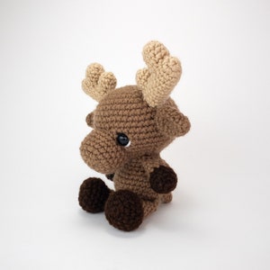 May include: A brown crocheted moose with large, tan ears. The moose has black eyes and brown crocheted feet.