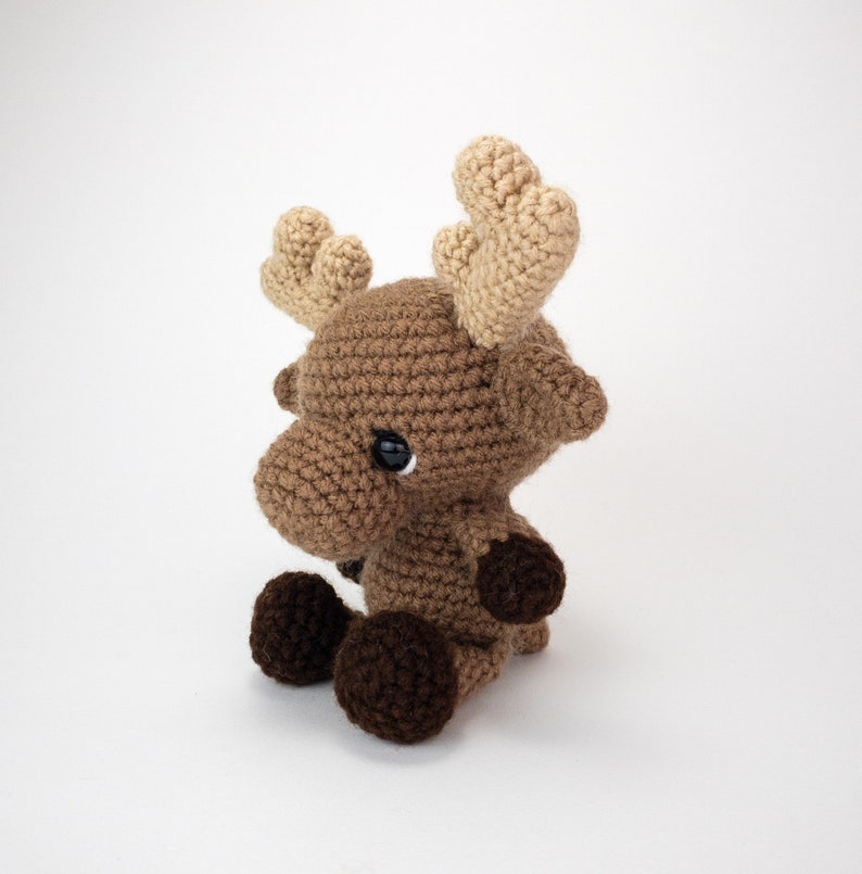 May include: A brown crocheted moose with large, tan ears. The moose has black eyes and brown crocheted feet.