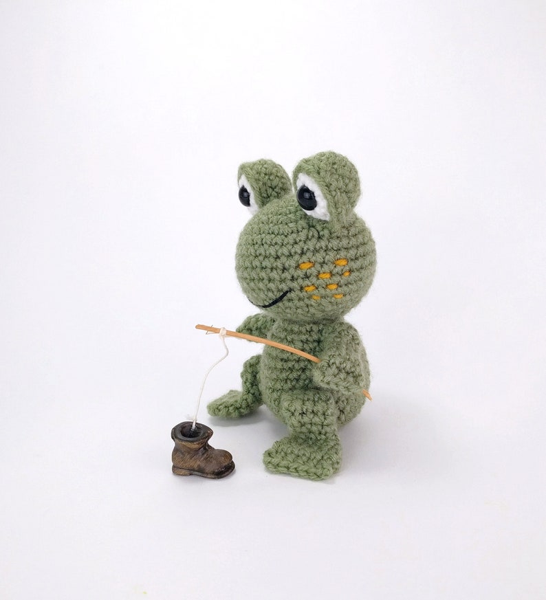 May include: A green crocheted frog toy holding a wooden fishing rod with a white string attached to a small brown boot.