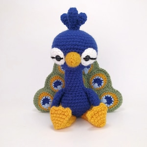 May include: A blue crocheted peacock plush toy with a green, blue, and yellow patterned tail. The toy has large white eyes and a yellow beak.