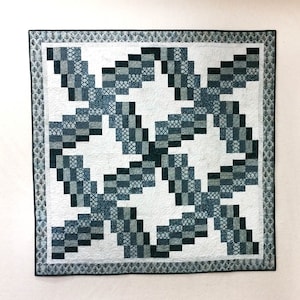 Może przedstawiać: Kołdra z białym tłem i ciemnoniebieskim i zielonym geometrycznym wzorem. Wzór składa się z kwadratów i prostokątów i tworzy efekt wirowania.