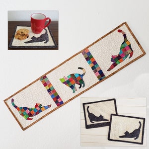 May include: A quilted cat-themed table runner and matching placemats. The runner features three colourful patchwork cat silhouettes on a cream background with a brown border. The placemats and a mug with cookies are also visible.