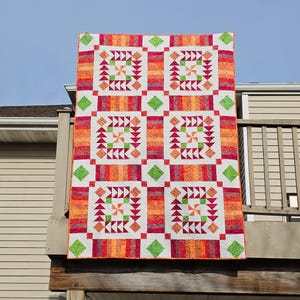 May include: A rectangular quilt featuring a repeating pattern of six blocks. Each block contains a central pinwheel surrounded by red and orange triangles on a white background. The quilt is bordered by vertical stripes of red, orange, and yellow.